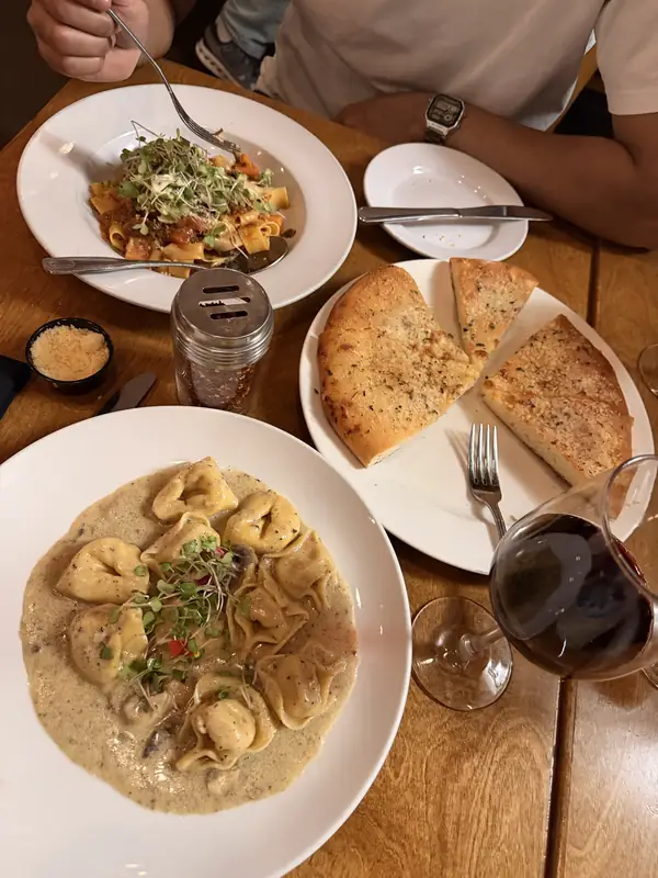 Pasta, garlic bread and red wine on a wooden table at Nonna + Zucchero.